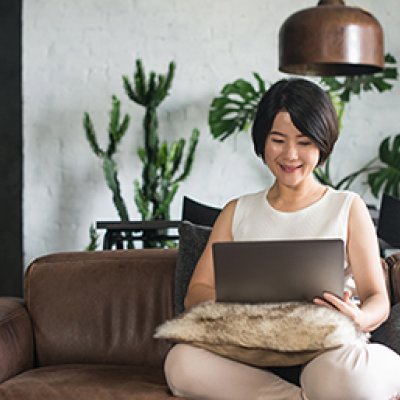 A smiling woman sitting on a couch using a laptop